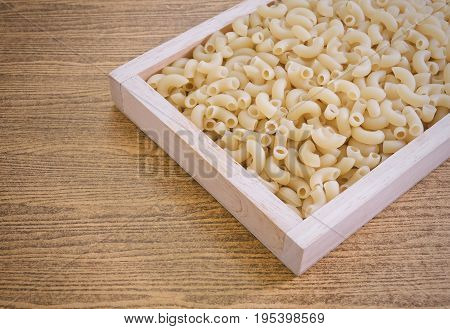Food and Cuisine Uncooked and Dried Elbow Macaroni or Gomiti Pasta in A Wooden Tray.