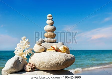 Rock zen of white stones shells and coral on a background of the summer sea and blue sky. Concept of harmony and balance.