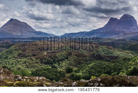 Assynt Peninsula Scotland - June 7 2012: Wild green and brown land seen from B869 near Achmelvich shows old mountain peaks under heavy gray and dark cloudscape.
