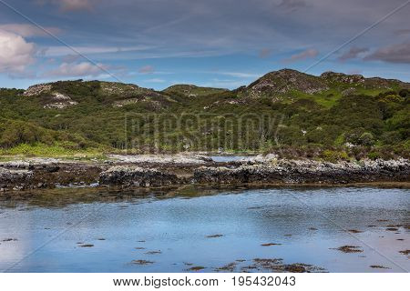 Assynt Peninsula Scotland - June 7 2012: Green rough hills and blue Atlantic Ocean waters of inlet South of Loch An Arbhair. Blue cloudy sky.