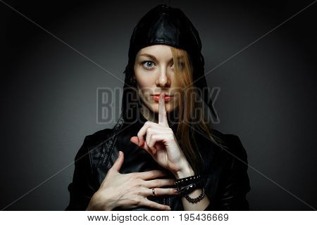 Young woman with red hairs gesturing for being quiet, shows silence sign hand on heart in dark background