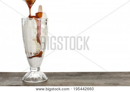 Pouring caramel sauce onto vanilla ice cream in dessert glass against white background
