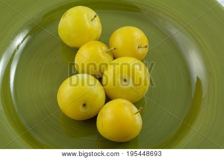 Close up of ripe yellow shiro plums on green plate