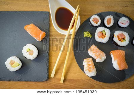 Sushi on a wooden table on black slate plate with soy sauce and chopsticks