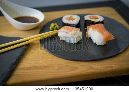 Sushi on a wooden table on black slate plate with soy sauce and chopsticks