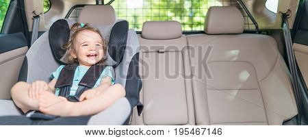 Beautyful smiling baby girl fastened with security belt in safety car seat