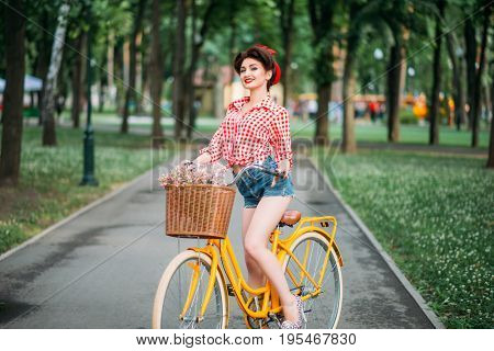 Pinup girl on retro bicycle with backet of flowers
