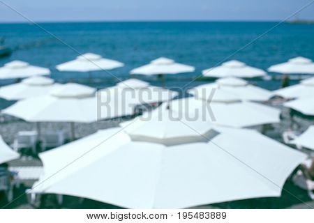 White beach umbrellas against blue sea and sky. Summer vacation concept. Exotic travel destination. Shot deliberately out of focus to serve as background. Horizontal