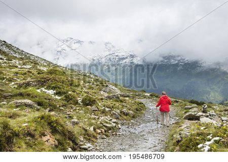 A female senior hiker wearing a red coat hiking in the Paznaun Valley near Galtur in Austria.