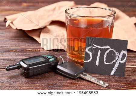Alcohol beverage, car keys, note. Brown alcohol beverage in glass, car keys, message stop on wooden background. How to stop alcohol drinking concept.