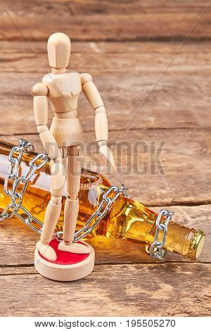 Alcohol bottle wrapped with metal chain. Human wooden dummy, bottle with chain, wooden background. Concept of alcohol addiction.