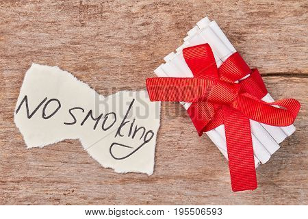 Pile of tobacco cigarettes and red bow. Message no smoking, cigarettes wrapped in red ribbon as gift.