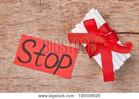 Pile of cigarettes with bow as gift. Message stop, cigarettes with filter and red ribbon, wooden background.
