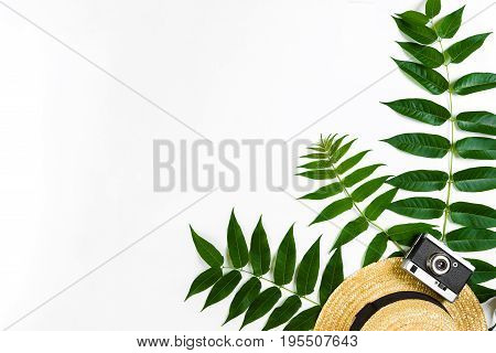 Straw hat with green leaves and old camera on white background, Summer background. Top view. Copy space. Still life. Flat lay