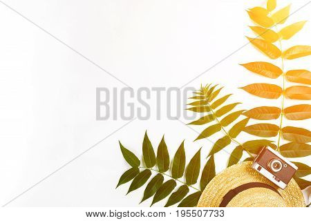 Straw hat with green leaves and old camera on white background, Summer background. Top view. Copy space. Still life. Flat lay. Sun flare