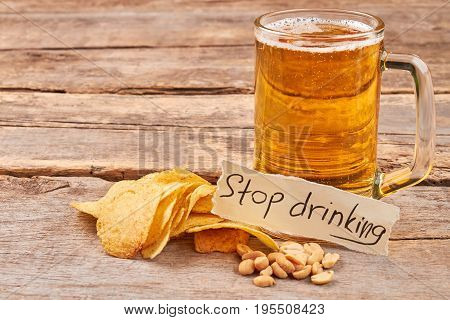 Stop drinking beer concept. Potato chips, peanuts, mug of beer, note, old wooden table.