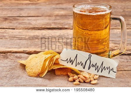 Beer addiction leads to heart disease. Potato chips, nuts, transparent mug of beer, image of heartbeat, wooden table.
