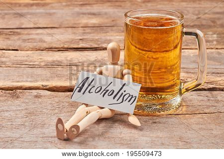 Alcoholism kills organism. Human wooden dummy with paper message near mug with beer.