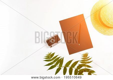 Straw hat with green leaves and old camera on white background, Summer background. Top view. Copy space. Still life. Flat lay. Sun flare
