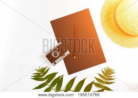 Straw hat with green leaves and old camera on white background, Summer background. Top view. Copy space. Still life. Flat lay. Sun flare
