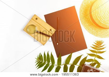 Straw hat with green leaves and old camera on white background, Summer background. Top view. Copy space. Still life. Flat lay. Sun flare