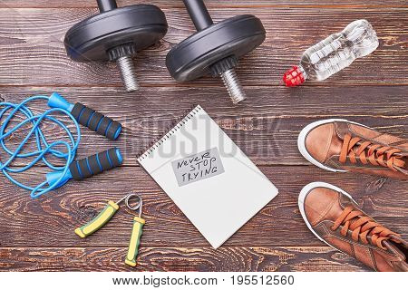 Never stop rtying message. Paper notebook in center of gym equipment, top view.