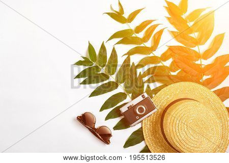 Straw hat with green leaves and old camera on white background, Summer background. Top view. Copy space. Still life. Flat lay. Sun flare