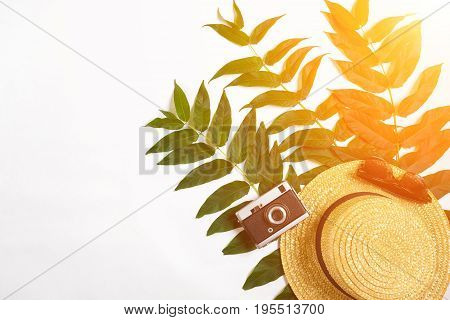 Straw hat with green leaves and old camera on white background, Summer background. Top view. Copy space. Still life. Flat lay. Sun flare