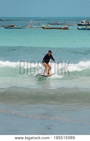 10/06/2017 Pantau Mawun Lombok Indonesia. Young woman learns to surf on a long board on learner waves in a paradise location.