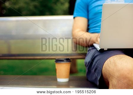 Freelance work. Casual dressed man sitting at wooden beanch inside garden working on computer.