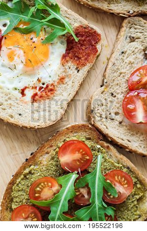 Vertical photo of healthy toasts with multicereal bread cherry tomato egg arugula pesto sauce tomato sauce on wooden table