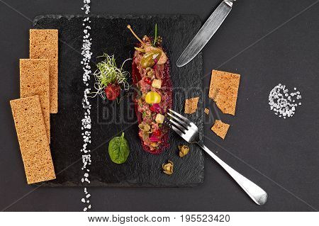 fresh beef tartar with salt and herbs and Crispbread, studio shot. Meat tartar on black shale. Top view