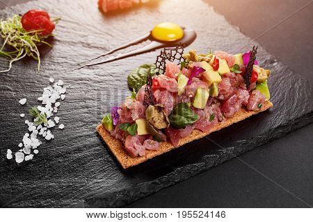 fresh tuna tartar with salt and herbs, studio shot. Fish tartar on black shale. Close-up
