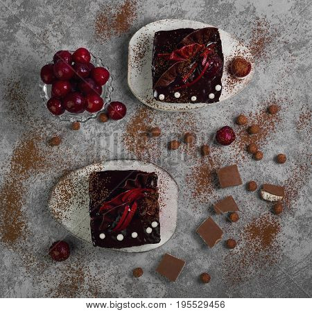 Chocolate cheesecake layered brownies cakes with with dark cherries and cherry sauce. Ingredients for Chocolate cherries cakes Pieces of chocolate and fresh cherries. Gray stone background. Top view.