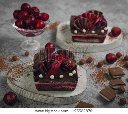 Chocolate cheesecake layered brownies cakes with with dark cherries and cherry sauce. Ingredients for Chocolate cherries cakes Pieces of chocolate and fresh cherries. Gray stone background.