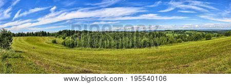 Bright summer rural landscape panorama with mown meadow hills forest blue sky and white clouds at nice sunny day. Fodder billet preparation for farm animals - agricultural concept