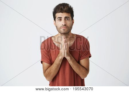Handsome attractive disappointed guy pledging for something. Man holding hands in prayer hoping for fortune. Sad boy telling sorry and making promises to his girlfriend.