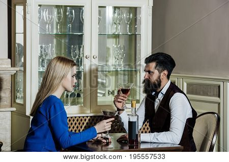 Girlfriend and boyfriend drinking red wine in restaurant. Girl or woman and man or hipster sitting with martini glasses at table. Couple in love. Date dating. Alcohol appetizer. Addictive convive