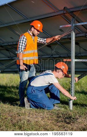 Builders installing frame with solar panels on helical pile. Engineers setting screw piles for solar power station.
