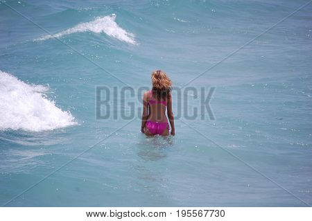 young woman wearing pink bikini wading in the ocean before wave hits her.