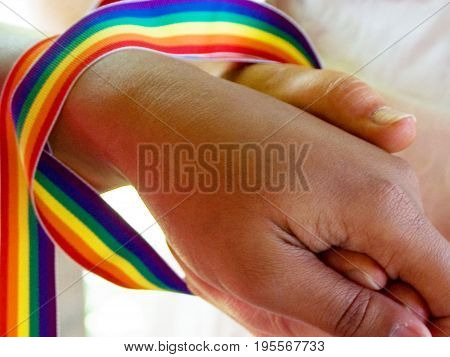 Newly Married Lesbian Couple holding hands with gay pride colors draped over and around their wrists.