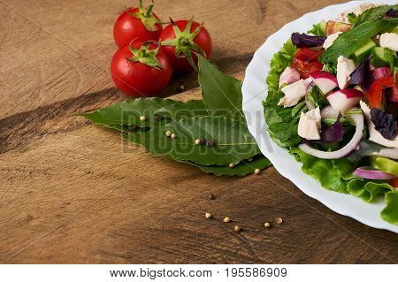 Fresh salad with chicken breast radish cucumber tomato onion bell pepper basil mint and other spices on old rustic wooden table. Copy space. Healhy eating