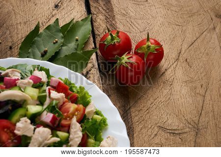 Fresh salad with chicken breast radish cucumber tomato onion bell pepper basil mint and other spices on old rustic wooden table. Copy space. Healhy eating. Top view