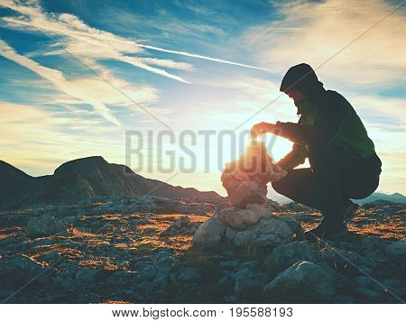 Alone Adult Man Is Stocking Stone To Pyramid.alps Mountain Summit, Evening Sun At Horizon.