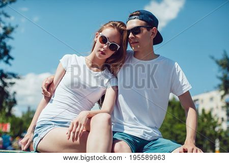 Young couple in white T-shirts sitting on the street. Mock up.