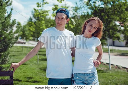 Young couple in white T-shirts standing in park. Mock up.