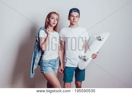 Young skater boy and girl with skateboard in white T-shirts standing on white background.