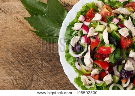 Healthy salad plate with bell pepper tomatoes chicken cucumder onion and mixed greens lettuce parsley on wooden background. Food and health.