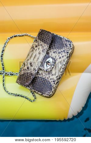 Fashion luxury snakeskin python handbag on a Inflatable Yellow Mattress in Swimming Pool.