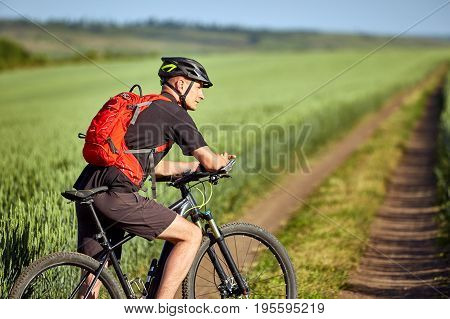 Young cyclist has adventure on a bike on green field with red backpack. Active life concept